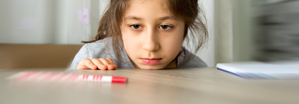 Girl with chin on table staring at marker.